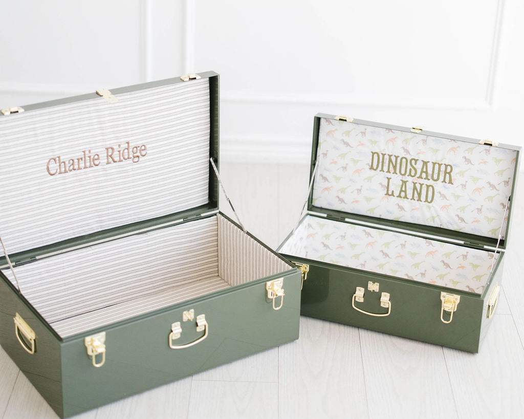 Green keepsake trunks open side by side, Charlie Ridge and Dinosaur Land stitched inside the lids