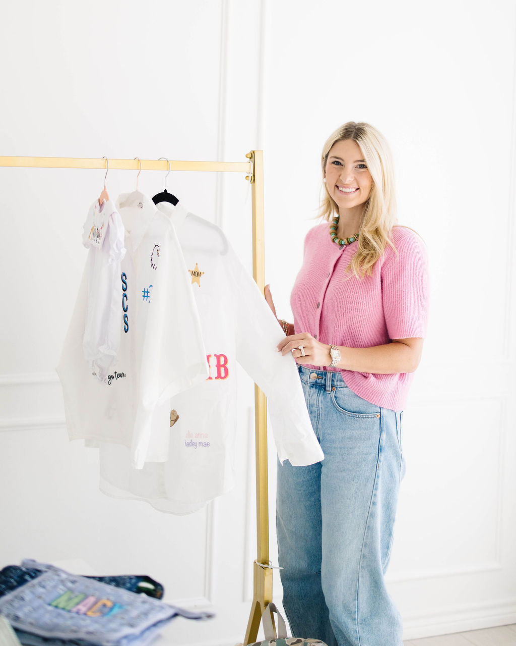 Madison beside a gold clothing rack of white All The Things shirts embroidered with monograms and icons