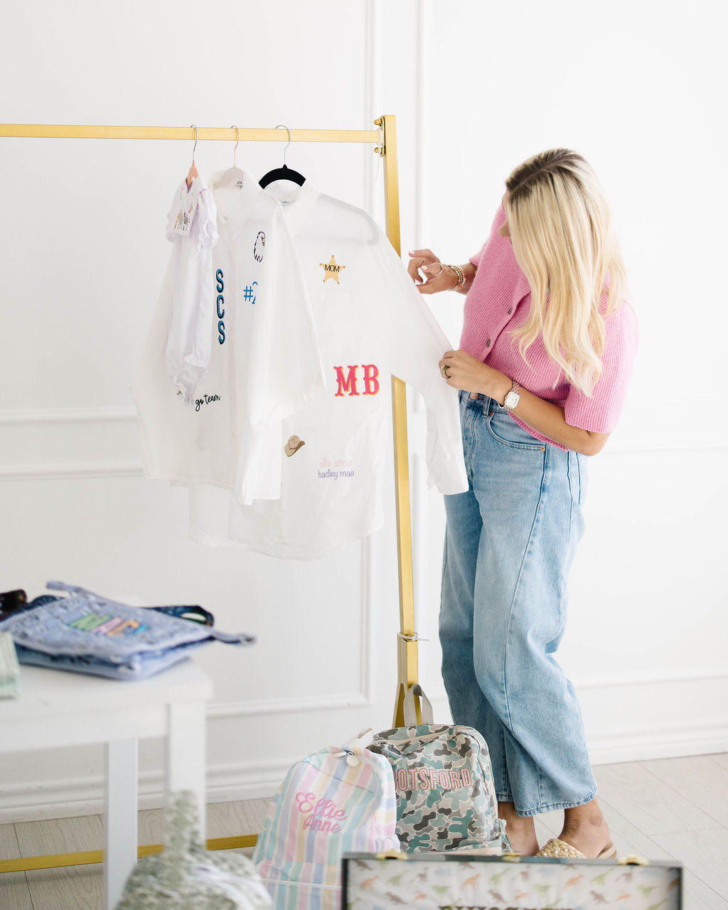 Madison adjusting an All The Things shirt with a red MB monogram and a gold sheriff star on a clothing rack