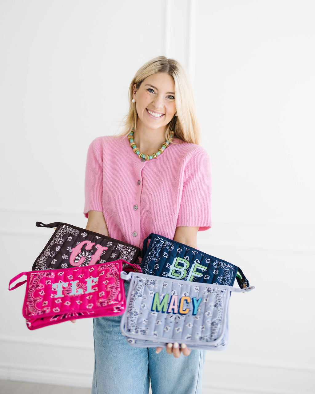 Madison holding bandana bags monogrammed CJ, BF, TLF and MACY against a white paneled wall