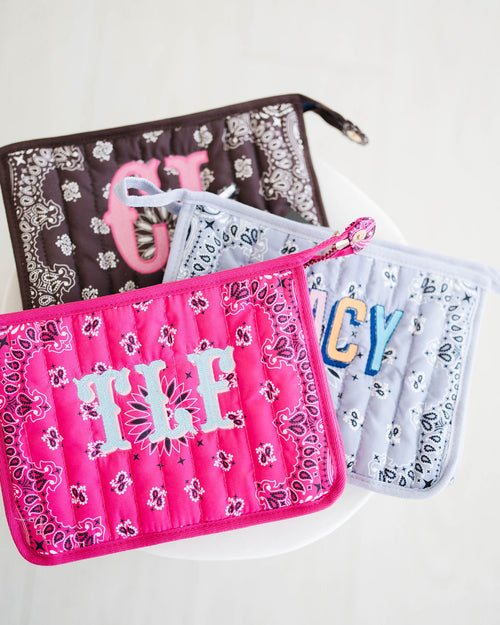 Pink quilted bandana bag with a light blue TLF monogram, brown and light blue bandana bags behind it