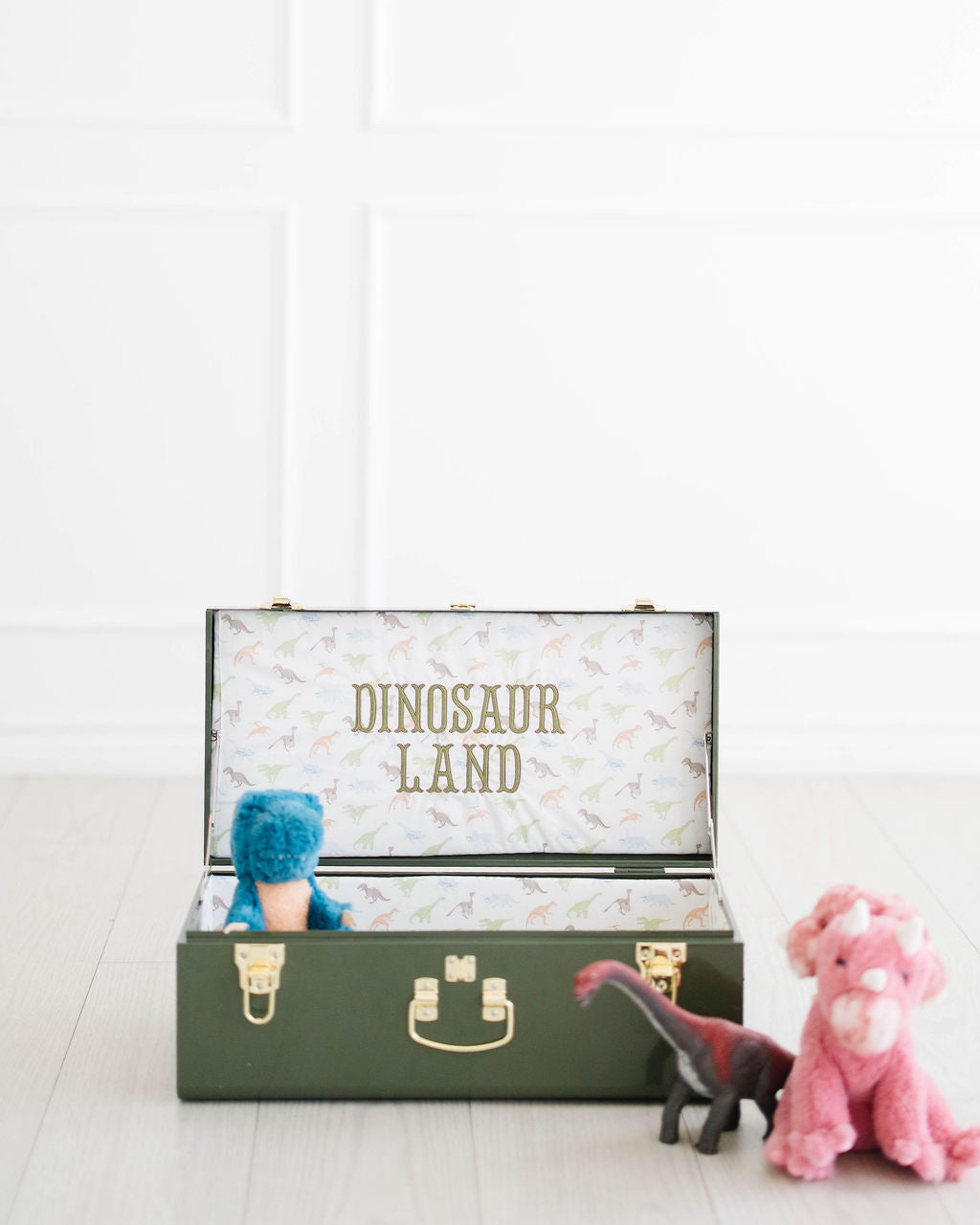 Open green keepsake trunk with Dinosaur Land stitched inside the lid, next to stuffed dinosaurs