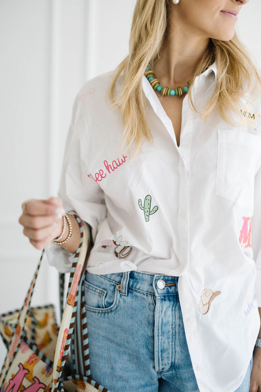 Close up of a white All The Things shirt embroidered with yee haw, a cactus, a cowboy hat and a pink monogram