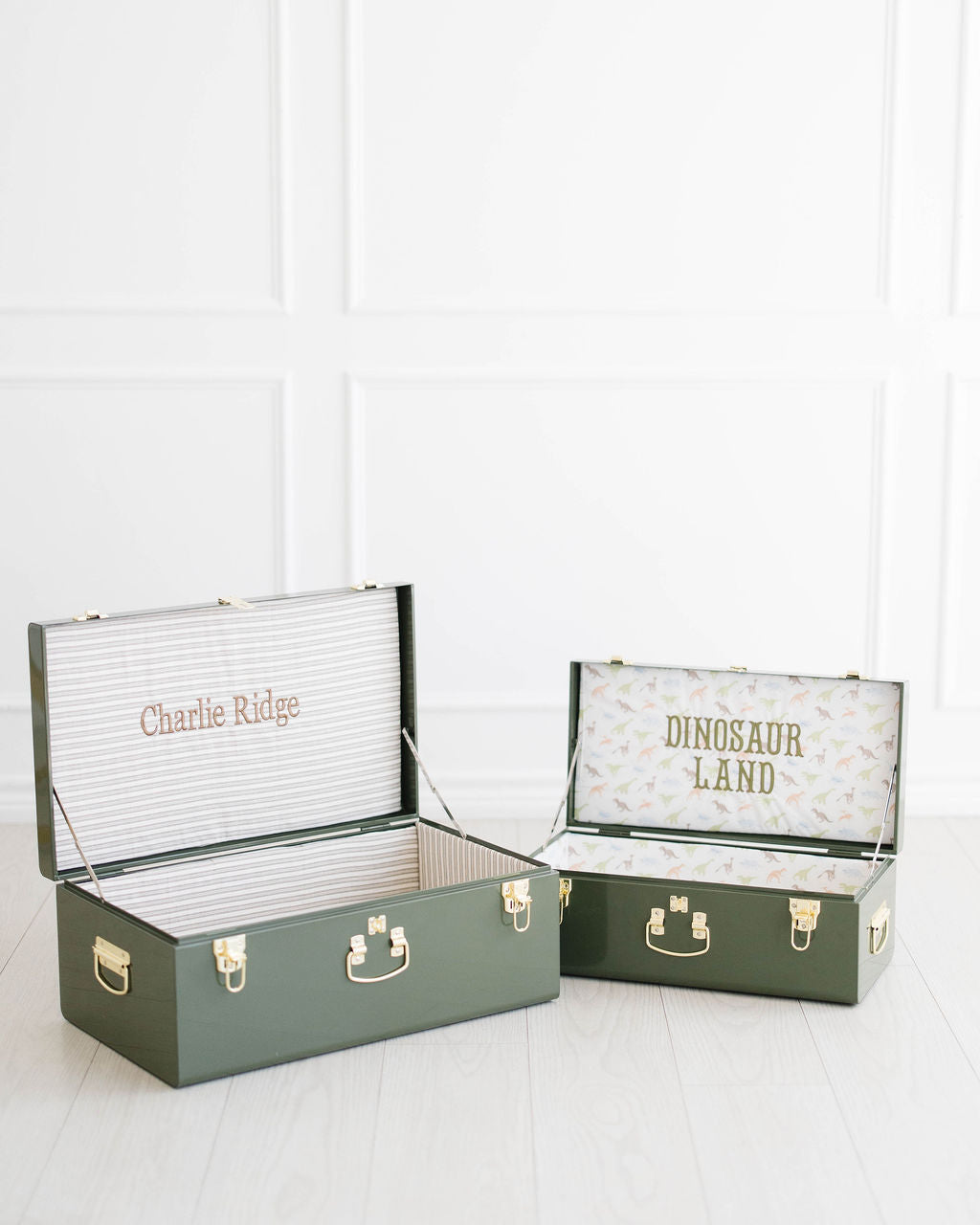 Large and Small green keepsake trunks open, stitched Charlie Ridge and Dinosaur Land inside the lids