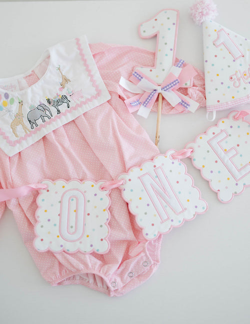 First birthday bundle: polka dot ONE banner, number one cake topper and party hat with a pink romper