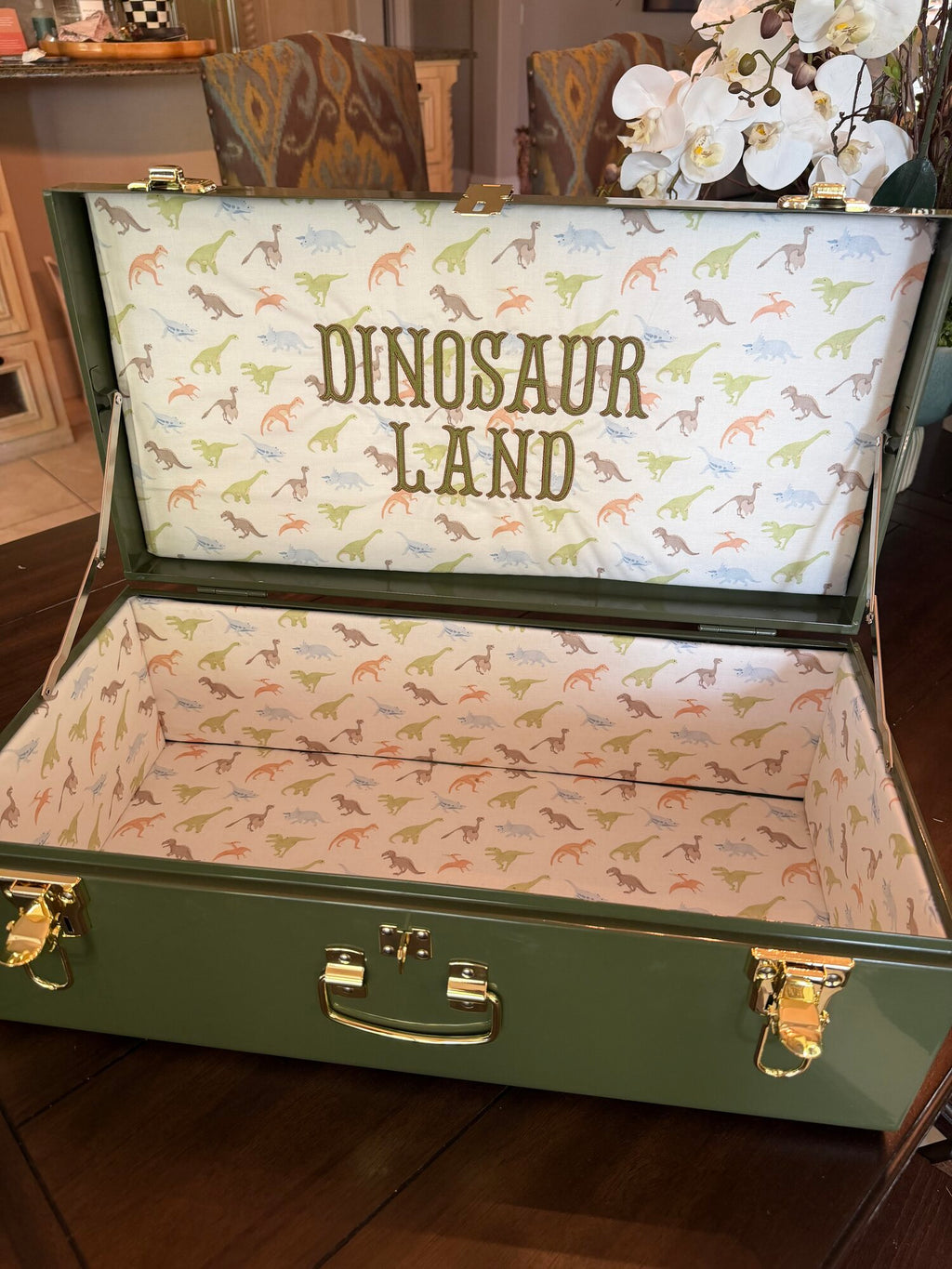 Green keepsake trunk lined in dinosaur fabric with Dinosaur Land stitched inside the lid